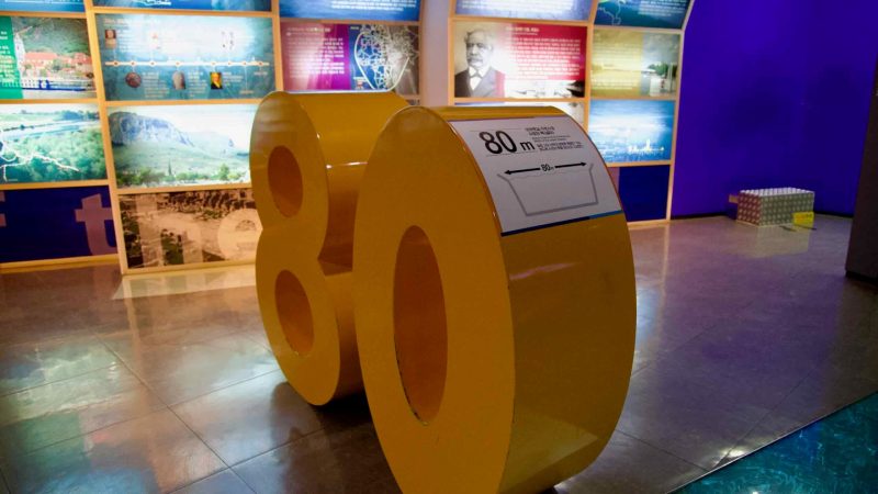 A bold yellow sculpture shaped like the number 80 inside the Ara Waterway Exhibition Hall.