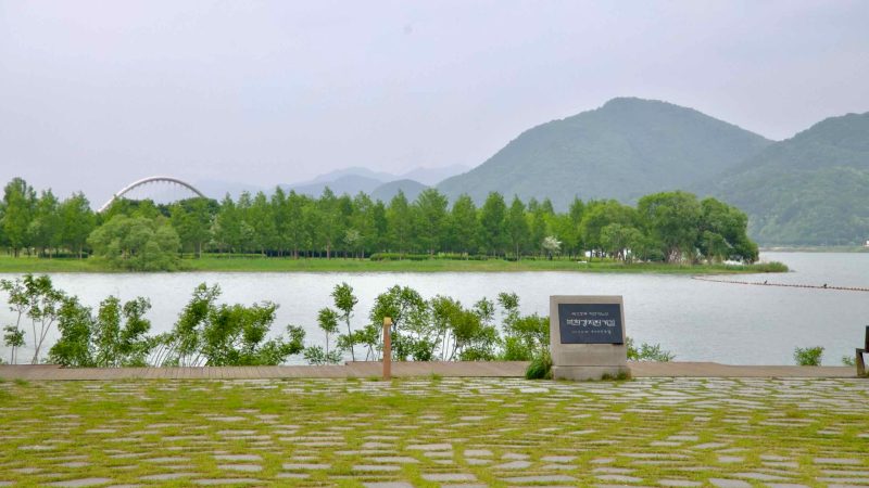 Looking across the North Han River from Balgeun Gwangjang toward Namyangju Water Garden, with Baetnari Bridge and forested hills forming a serene riverside backdrop.