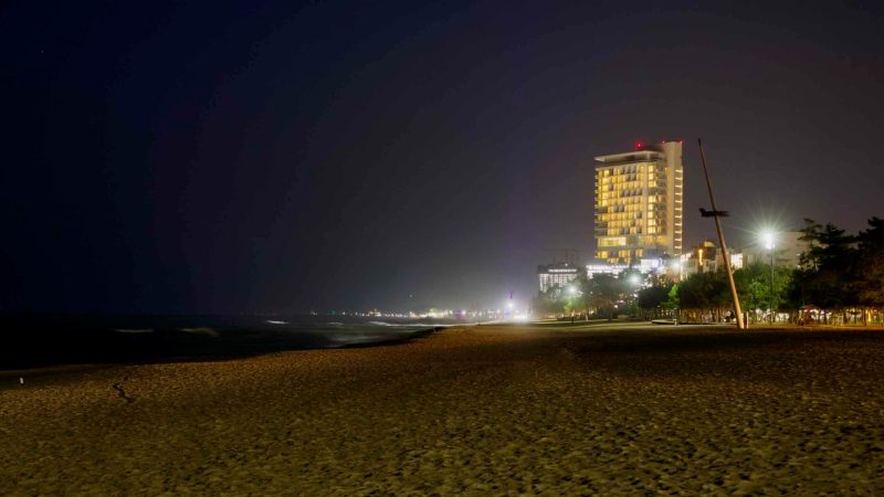A nighttime view of Gyeongpodae Beach with the Seamarq Hotel illuminated in the distance. The peaceful, dimly lit shoreline highlights the tranquil ambiance of the coastal scene.
