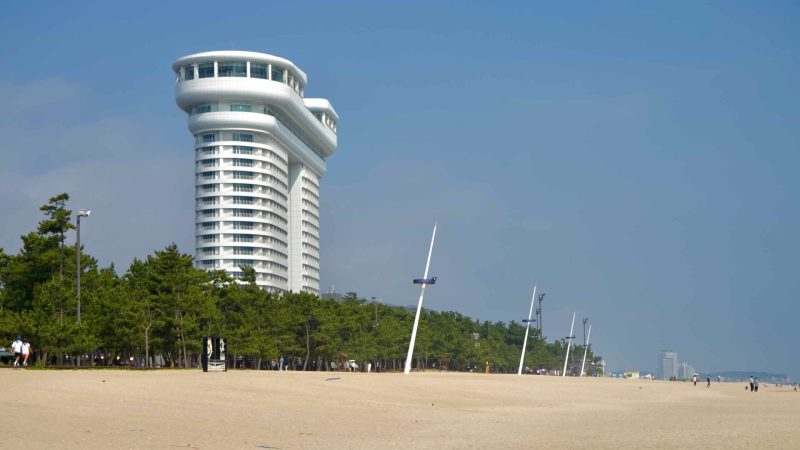 White tower overlooks Gyeongpodae Beach, where visitors enjoy the sandy shoreline.