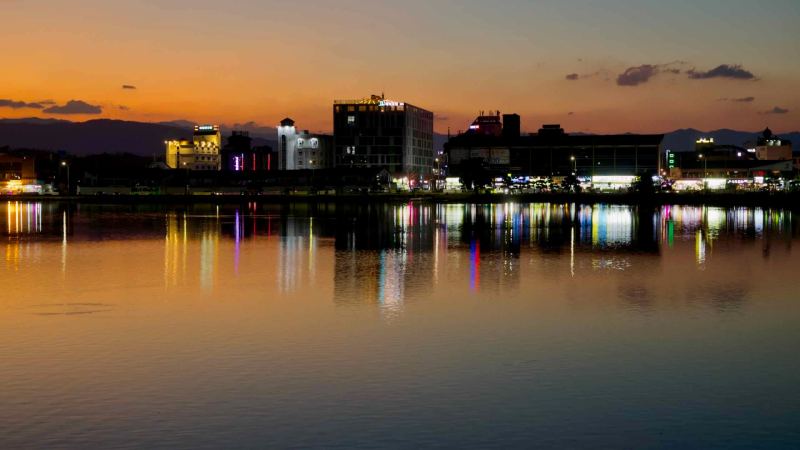 A view of Gyeongpodae Lake at sunset with reflections of city lights in Gangneung.