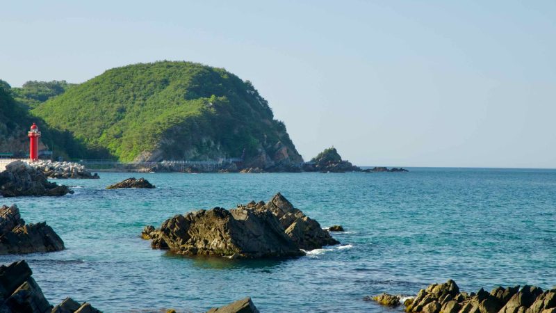 The rocky coastline of Simgok Port and Heonhwa Road with its distinctive red lighthouse.