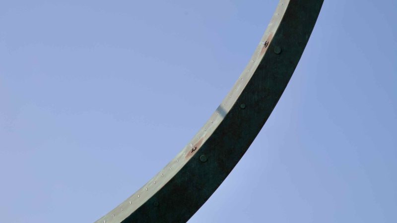 Jeongdongjin hourglass monument's curved edge silhouetted against a cloudless blue sky.