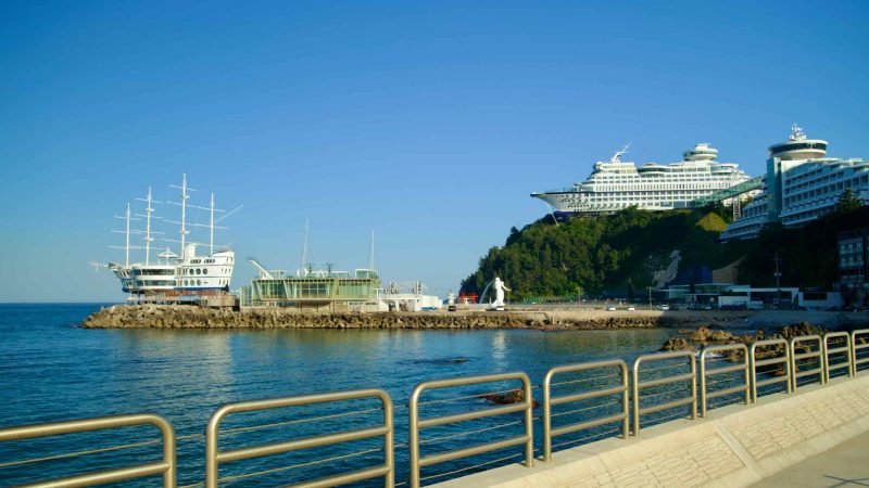 A view of Jeongdongjin Port featuring the distinctive tall ship restaurant Fish Soup and the iconic Sun Cruise Resort perched on the hillside.