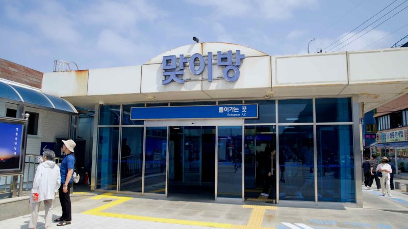 Passengers walk near the platform entrance of Jeongdongjin Station, marked by blue glass doors and signs.