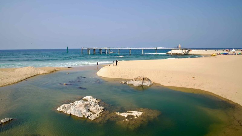 Shallow stream curves through golden sand toward the East Sea, with a narrow pier near Jeongdongjin Beach.