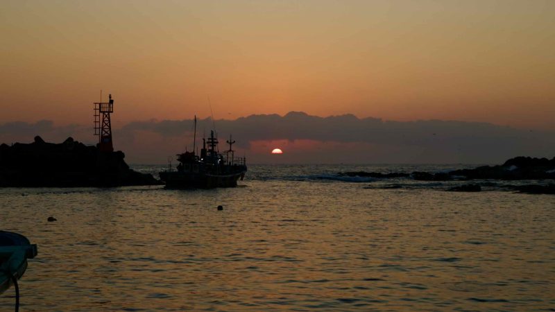 A sunrise at Muam Port as a fishing boat heads out to sea.