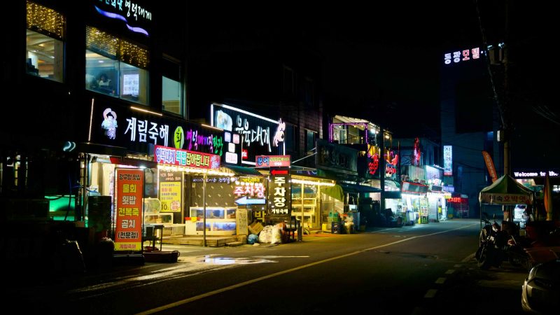 A closer look reveals the vibrant details of snow crab restaurants at night in Ganggu Port, with their lights warmly illuminating the surrounding area.