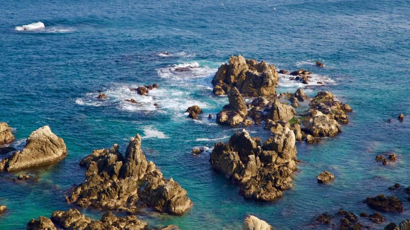 A rugged coastal rocky outcrop beside Haesindang Park, with waves energetically crashing against the rocks in the shallow waters of the East Sea.