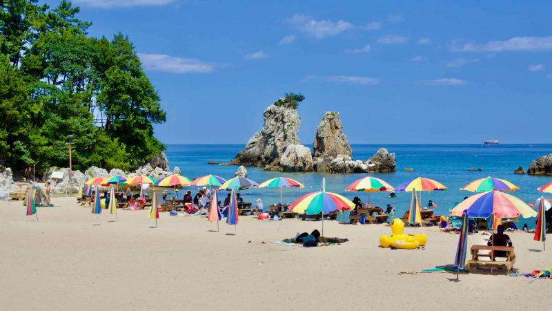The picturesque Huam Beach, adorned with multicolored parasols on its sandy expanse, offers a stunning view of the iconic Chuam Candlestick Rock and tall rocks emerging from the East Sea.