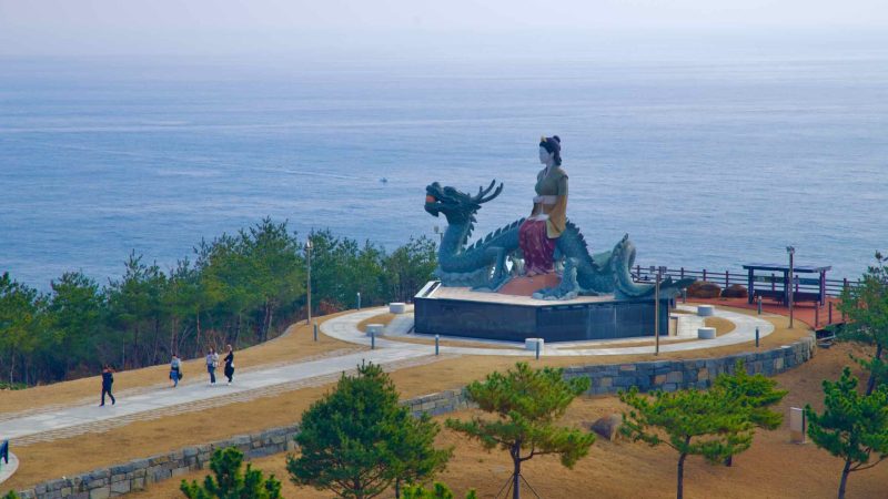A view of the large Lady Suro sculpture with a path leading to it, and the East Sea in the background, at Lady Suro Memorial Park.