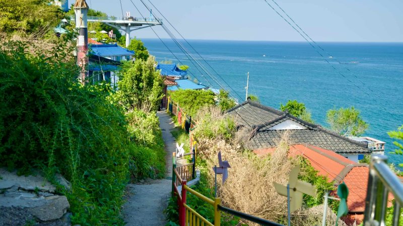 A pathway on Nongoldam Street leads down to traditional homes with blue and red rooftops, offering views of the East Sea.