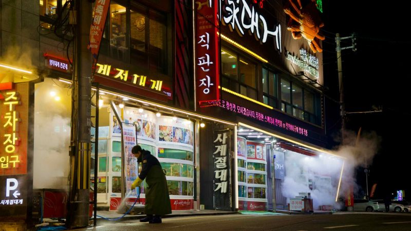 A worker sprays the storefront with a hose outside the three-story snow crab restaurant in Ganggu Port, maintaining the cleanliness and inviting appearance.