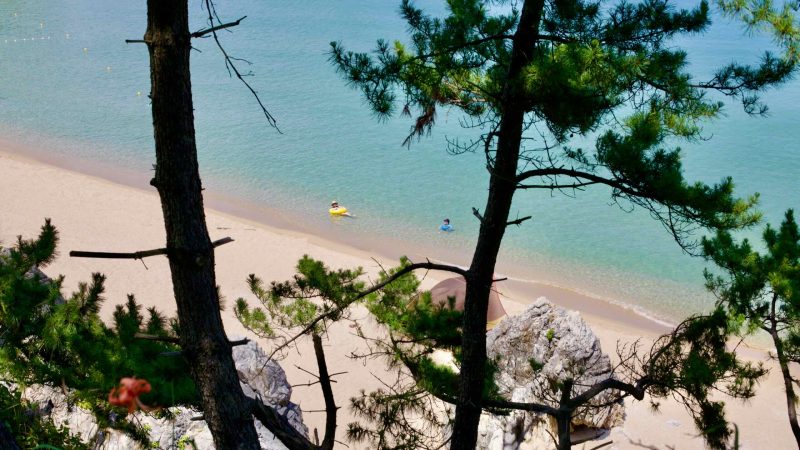 Two swimmers are seen enjoying the tranquil waters of Chuam Beach, floating gently in the clear blue expanse of the East Sea, embodying the essence of a peaceful summer day.