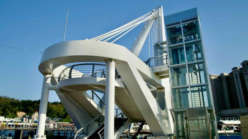 Entrance stairs and elevator to the Daepo Skywalk, a pedestrian bridge and viewing platform over Daepo Port, offering scenic views and glass-floor sections above the water.