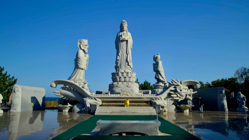 The Avalokitesvara statue stands atop an intricately carved dragon base, flanked by attendant figures, creating a serene spiritual setting at Huyuam Hermitage.