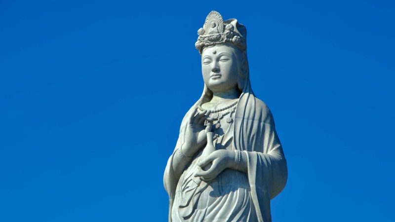 A close-up of the Seawater Avalokitesvara statue at Naksansa Temple, with visitors exploring its serene surroundings under a clear blue sky.