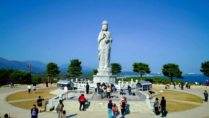 The Seawater Avalokitesvara statue stands as a sacred and iconic symbol at Naksansa Temple, surrounded by visitors and panoramic views of the East Sea.