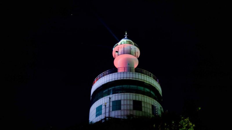 A night view of the top of Sokcho Lighthouse, bathed in pink lights against a black sky, symbolizing maritime guidance and the city's coastal heritage.