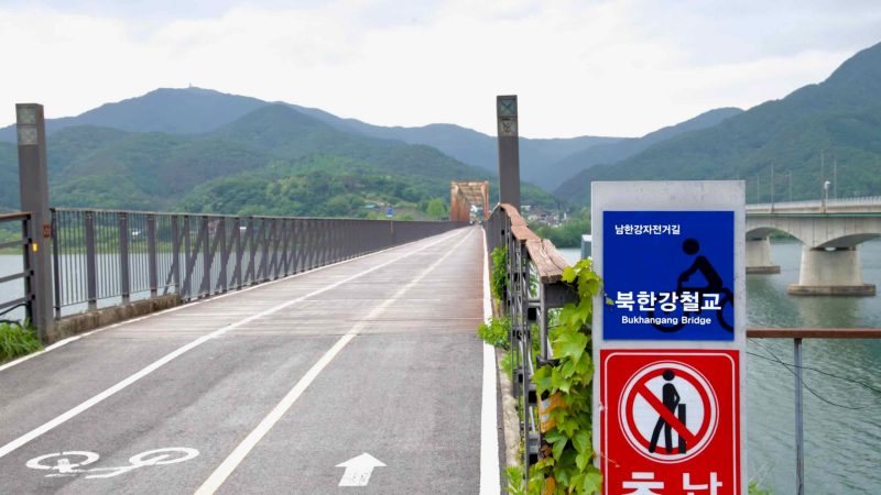 A signpost marks the entrance to the Bukhangang Bridge bike path, a former railway bridge now connecting cyclists across the North Han River.