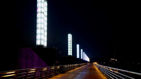 A nighttime view down the top deck of Yeoju Weir shows a line of illuminated pillars modeled after a water clock, glowing over the bike and pedestrian path.