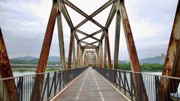 Rusted steel beams frame the old Bukhangang Railroad Bridge, now repurposed as a bike and pedestrian path above the North Han River.