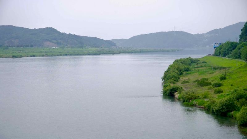 A stretch of the South Han River flows past green hills and riverbanks, viewed from Ipo Weir.
