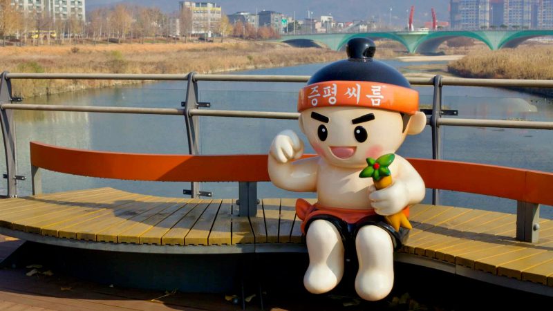 A statue of a Korean ssireum wrestler on a bench on a bridge in Baekro Park.