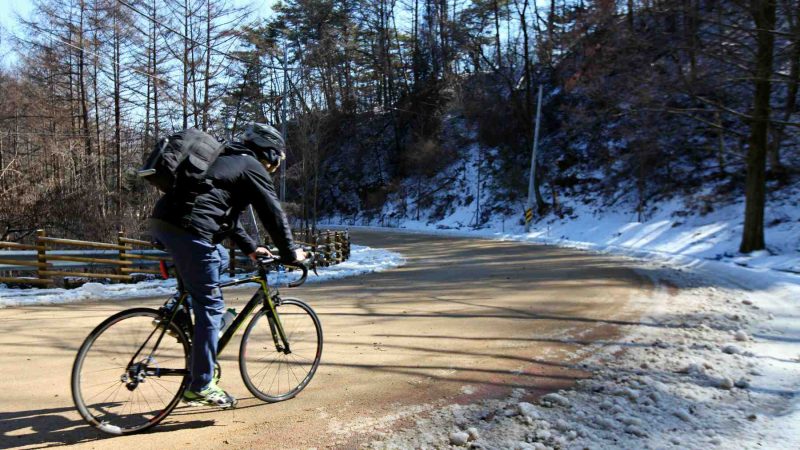A picture of a cyclist riding down the snowy Ihwa Pass (이화령) on the Saejae Bicycle Path in Goesan County, South Korea.