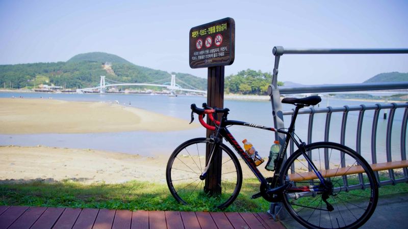 A bike rests against a railing at Baealdo Waterfront Park, overlooking the Seomjin River and Haemaji Bridge..