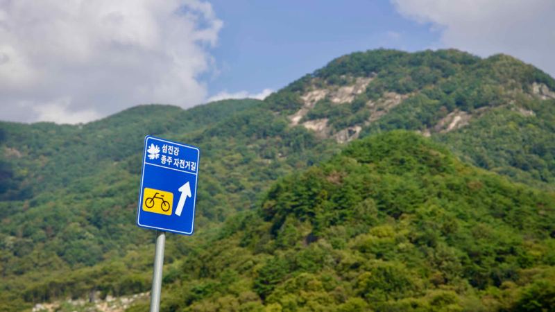 A blue sign marks the Seomjingang Bike Path’s route near the rocky slopes of Muryang Mountain.