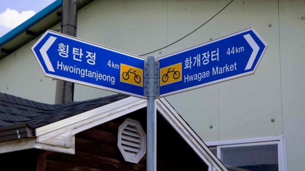 A directional signpost marks cycling distances to Hwoingtan Pavilion and Hwagae Market.