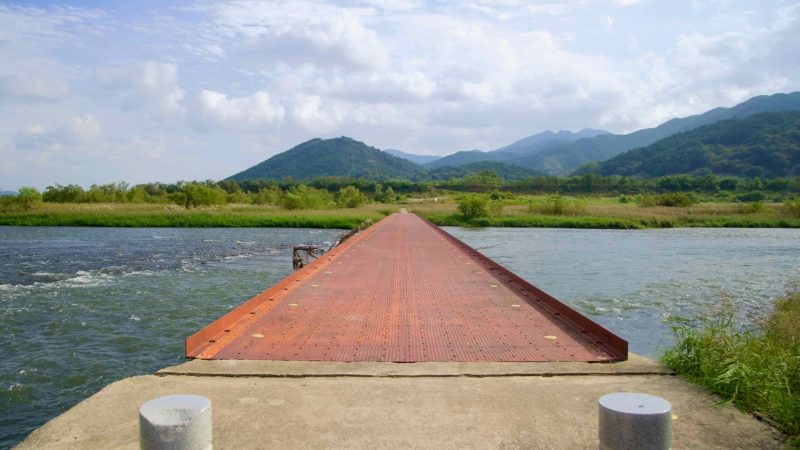 An iron bridge spans the Seomjin River, leading towards lush greenery and rolling mountains.