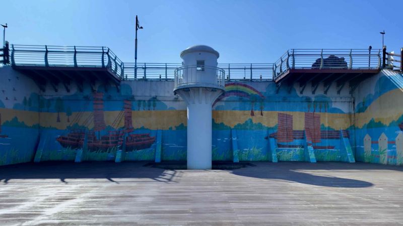 The Yeongsan Port Lighthouse stands against a vibrant mural illustrating the historic Hwangpo sailboats.